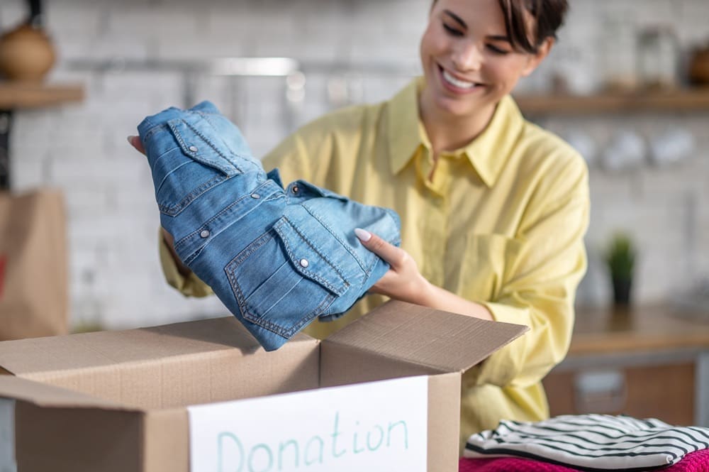 A person places folded denim jeans into a donation box labeled 